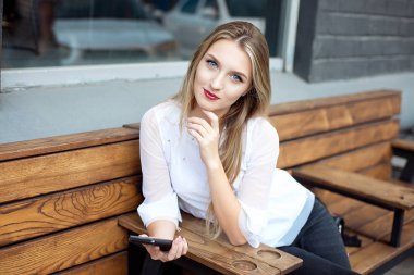 Bir kafe iç taşınabilir bir ağ kitabı ile otururken bir cep telefonu tutan genç güzel sarışın kadın, bir kafede dinlenirken bir cep telefonu kullanarak büyüleyici rüya gibi kadın.