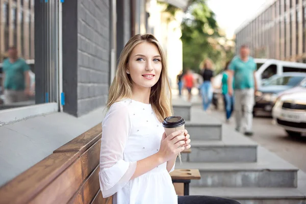 สาวสวยเดินในเมืองและดื่มกาแฟโดยร้านกาแฟกลางแจ้ง ฉากตอนเช้าของเมือง . — ภาพถ่ายสต็อก