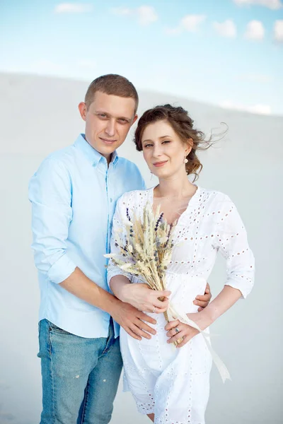 Jonge man en vrouw knuffelen op een achtergrond van wit zand, duinen. Liefdesverhaal in de leegte. — Stockfoto