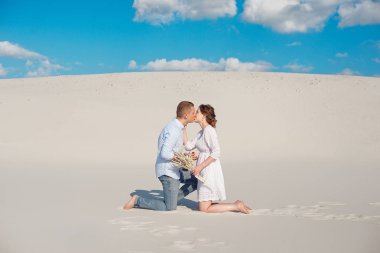 Yakışıklı adam kıza evlilik teklifi nde bulunduruyor, dizini büküyor, çölde kumun üzerinde duruyor. Aile hayatının mutlu anları.