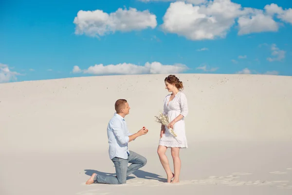 Gutaussehender Kerl macht dem Mädchen einen Heiratsantrag, beugt sein Knie und steht auf dem Sand in der Wüste. Glückliche Momente im Familienleben. — Stockfoto