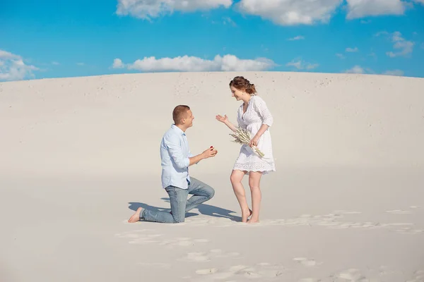 Gutaussehender Kerl macht dem Mädchen einen Heiratsantrag, beugt sein Knie und steht auf dem Sand in der Wüste. Glückliche Momente im Familienleben. — Stockfoto