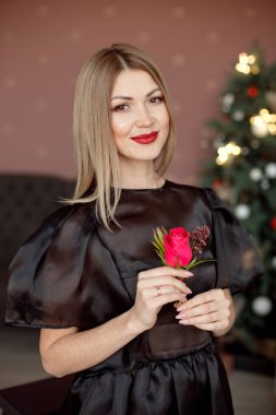 Mutlu yıllar sana. Siyah bir elbise ve parlak makyaj Yeni Yıl çelenk arka planda Noel kutlayan bir güzel genç kadın. Yeni yıl partisi. Noel Arifesi