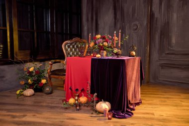 Mumlar ve kırmızı bir masa örtüsü üzerinde bronz bir vazo çiçek bir buket ile Halloween kabak dekor.