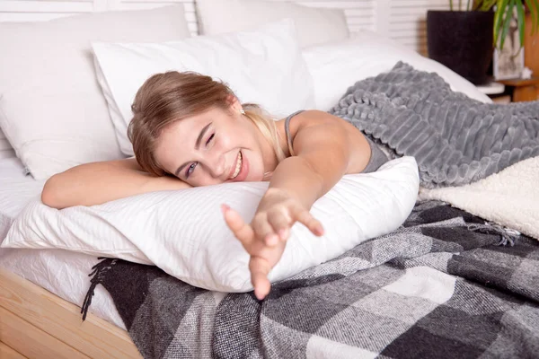Молодая счастливая девушка, сидящая на кровати по утрам, завернутая в белое одеяло, наслаждаясь утром . — стоковое фото