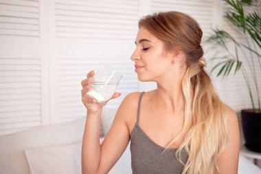 Beyaz kız yatakta sabah oturan suyu içer.