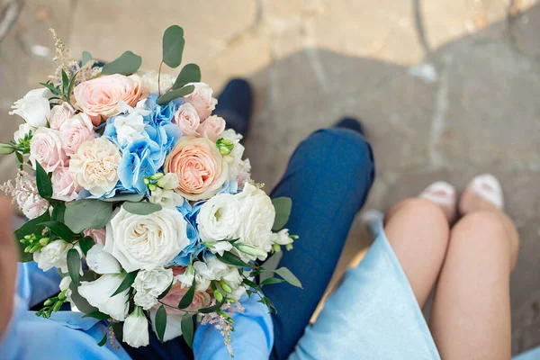 Primo piano della sposa e dello sposo, seduti su una panchina nel parco, lo sposo abbraccia la sposa, tenendo un bouquet nelle mani dell'aria aperta — Foto Stock