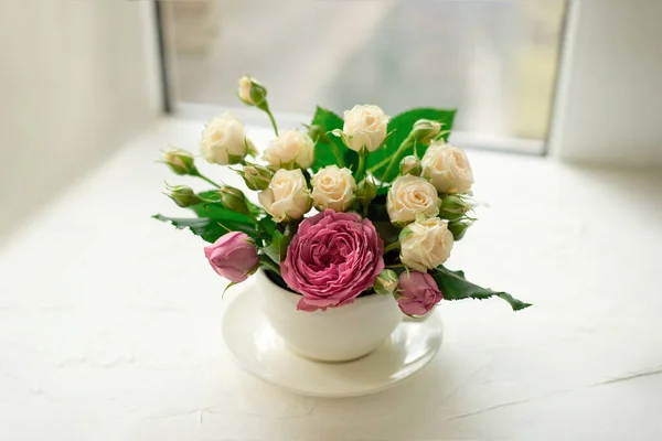 A bouquet of white roses in a cup on a white table opposite the window Royalty Free Stock Photos
