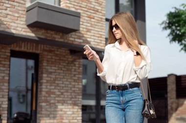 Beyaz gömlek ve patron gözlük yönetmen sevimli bir çekici çekici neşeli kız Portresi, iş merkezinin girişine yakın duran ve telefondan Sms arama