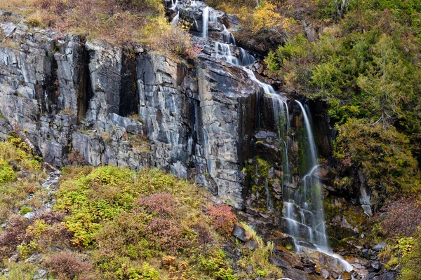 Una cascada en una ladera cubierta de coloridos árboles y arbustos otoñales — Foto de Stock