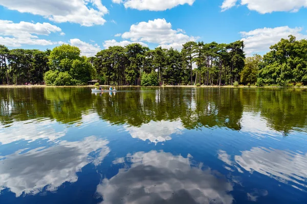 People boating on the lower lake in the Bois de Boulogne with clouds reflection on the lake - Paris, France