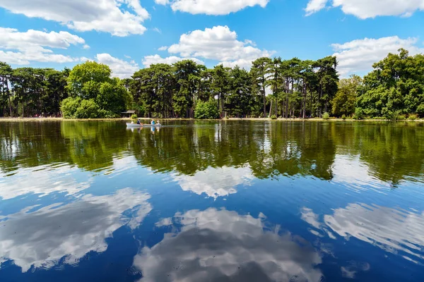 Bois de Boulogne 'da göl kıyısında yüzen insanlar göle yansıyan bulutlarla Paris, Fransa
