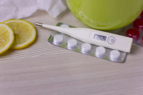 Limonlu bir fincan sıcak çay. Soğuk algınlığı ve grip tedavisi. Grip ilacı, termometre, hap ve kağıt mendil.