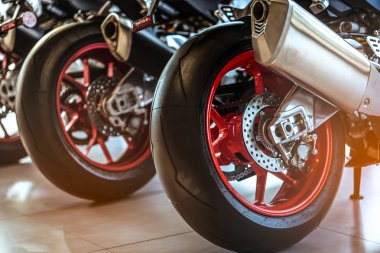 Closeup of new motorbike rear wheel . Big bike parked in showroom of dealership.  Motorcycle exhaust pipes. Iconic motorcycle with sports design. Black tire with unique pattern and red spoked wheels. clipart
