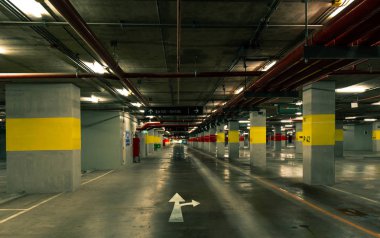 Perspektif görünümü boş kapalı araba park alışveriş merkezinde. Yeraltı beton geceleri açık lamba ile garaj otopark. Beyaz yön işareti. Hayatını yaşamak için bir yol seçin. Kablolama ve sıhhi tesisat.