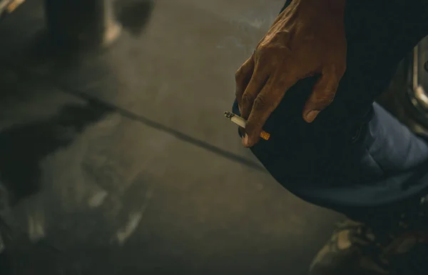 Asian man with dirty hand hold cigarette and smoke. Poor Asian men labor sit and smoking cigarette while take a break or after hard working. Nicotine addicted. Carcinogens causes lung cancer.