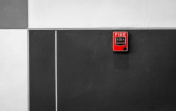 Fire alarm on black and white concrete wall. Warning and security system. Emergency equipment for safety alert. Red box of fire alarm on wall of school, hospital, factory, office, apartment, or home.