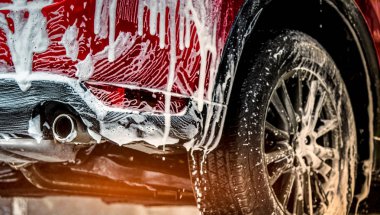 Red compact SUV car with sport and modern design washing with soap. Car covered with white foam. Car care service business concept. Car wash with foam before glass waxing and glass coating automobile. clipart