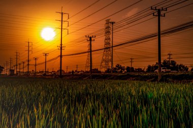 Güneş batarken yüksek voltajlı elektrik direği ve iletim hatları turuncu, kırmızı gökyüzü ve bulutlarla. Mimarlık. Gün batımında siluet elektrik direkleri. Güç ve enerji. Enerji korunumu.