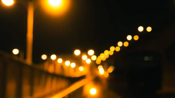 Blurred bridge, road, and electric pole with yellow bokeh in the night. Night life concept. Gold, white, and orange bokeh of lights in street. Lonely and alone in the night concept.