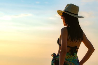Siyah mayo ve hasır şapka içinde mutlu Genç Asyalı kadın arkadan görünüm rahatla ve tatil tropikal cennet plaj günbatımında tadını çıkarın. Yaz tatil moda kız. Güzellik seksi modeli. Zarif yaşam tarzı