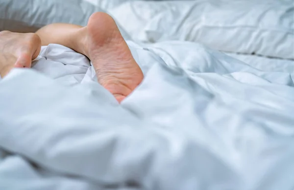 Close up woman bare feet on the bed  over white blanket and bed sheet in the bedroom of home or hotel. Sleeping and relax concept. Lazy morning. Barefoot of woman lying on white comfort bed and duvet.