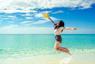 Mutlu genç kadın kum beach adlı atlama rahat tarzı moda ve saman şapkalı. Rahatlatıcı, eğlence ve tatil tropikal cennet plaj mavi gökyüzü ve beyaz bulutlar ile tadını çıkarın. Yaz tatili kız.