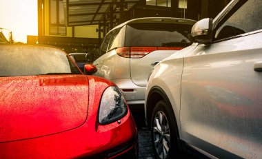 Kırmızı ve gümüş araba otelin açık beton otoparkta park, ev, ya da daire. Elektrikli veya hibrid otomobil teknolojisi. Kiralık iş için park yeri. Spor araba ve Suv araba raindrops.