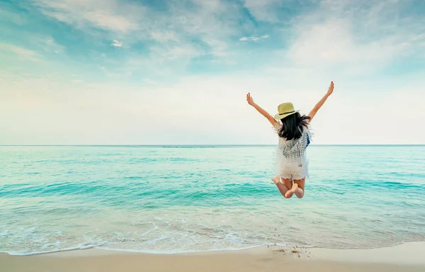 Mutlu genç kadın kum beach adlı atlama rahat tarzı moda ve saman şapkalı. Rahatlatıcı, eğlence ve tatil tropikal cennet plaj mavi gökyüzü ve beyaz bulutlar ile tadını çıkarın. Yaz tatili kız.