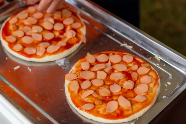 Man make pizza in kitchen with pizza crust and sliced sausage. Two pieces pizza on stainless steel tray. Fast food and junk food concept. Unhealthy food.