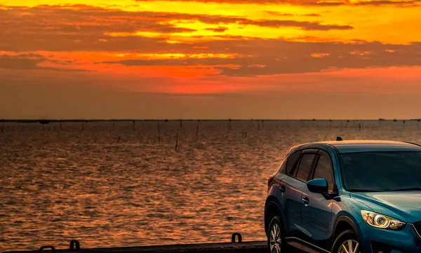 Sininen kompakti maastoauto, jossa urheilu ja moderni muotoilu pysäköity betonitielle meren rannalla auringonlaskun aikaan illalla. Hybridi- ja sähköautoteknologian käsite. Auton pysäköintipaikka. Autoteollisuus . — kuvapankkivalokuva