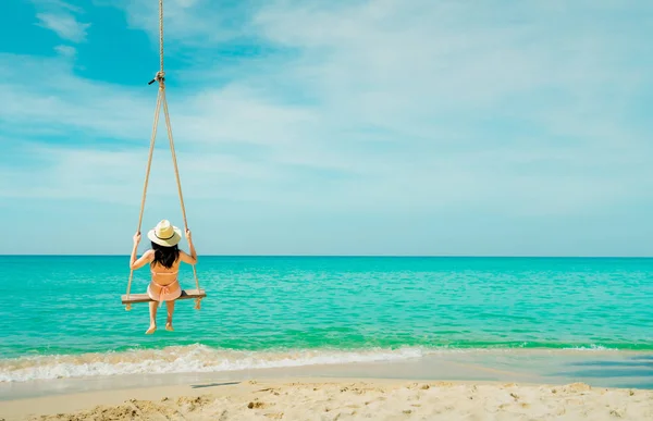 Donna asiatica indossare costumi da bagno e cappello oscillare le altalene sulla spiaggia di sabbia e cercando bellissimo paradiso tropicale mare e cielo nella giornata di sole. Vacanze estive. Vibrazioni estive. Ragazza godendo e rilassante in vacanza — Foto Stock