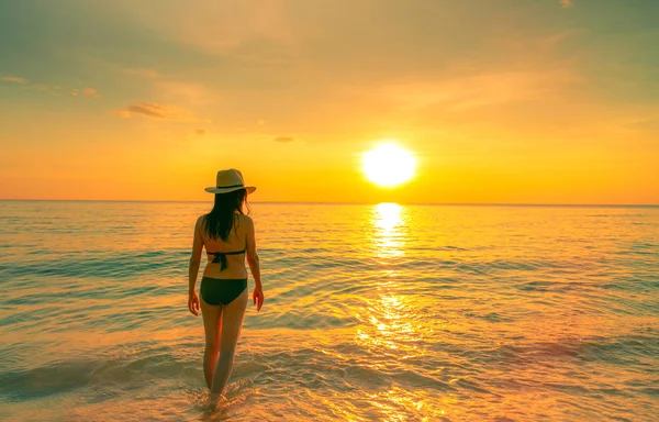剪影性感的女人走在热带海与美丽的日落天空在天堂海滩。快乐的女孩穿比基尼和草帽放松暑假。假日旅行。夏天的气氛。生活还在继续. — 图库照片