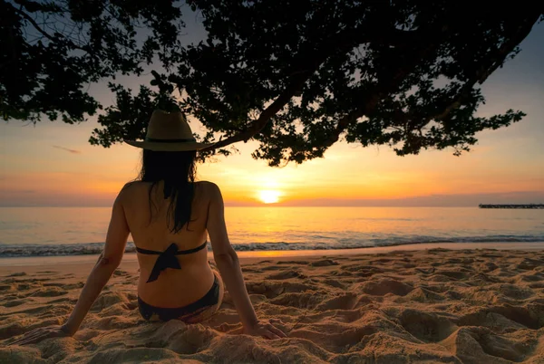 Baksidan på gravid kvinna sitta på sand och solnedgången på tropical beach. Kvinnan bär baddräkt och stråhatt avkopplande på tropical paradise beach på sommarlovet. Holiday resor ensam. — Stockfoto