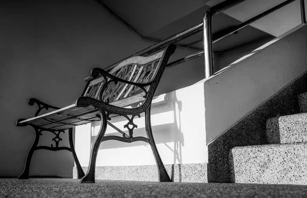 Empty wrought iron bench placed near stairs of the building. Sunshine in to the concrete building. Depressed, sad and lonely concept. One empty wrought iron bench. Interior furniture at apartment. — Stock Photo, Image