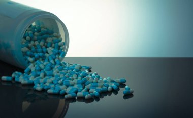 Mavi ve beyaz kapsül pill beyaz plastik şişe kapsayıcıdan döktüm. Küresel sağlık kavramı. Antibiyotik ilaç direnci. Antimikrobiyal kapsül hap. İlaç endüstrisi. Eczane.