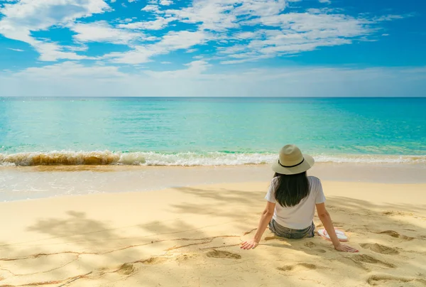 Glad ung kvinna i vita tröjor och shorts som sitter vid sandstrand. Koppla av och njuta av semester på tropiskt paradis strand med blå himmel och moln. Flicka i sommarsemester. Sommar vibbar. Glad dag. — Stockfoto