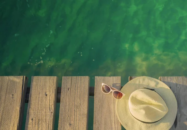 Ovanifrån av stråhatt och solglasögon på träbro över smaragd gröna havsvatten. Sommar semester resor bakgrund. Sommar vibbar. Coconut tree skugga i solglasögon. — Stockfoto