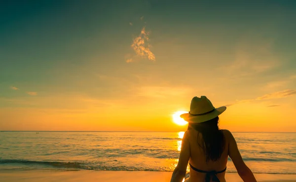 Bakifrån av asiatisk kvinna bära bikini och stråhatt sitta på sandstrand koppla av och njut av semester på tropical paradise beach. Kvinna titta vackra solnedgången. Sommarsemester. Resa ensam. Sommaren vibes. — Stockfoto