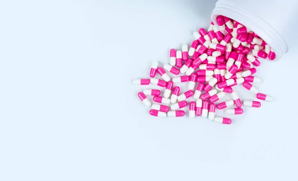 Roze-wit antibiotica capsule pillen verdeeld uit witte kunststof drug fles. Antibiotica drug weerstand concept. Gebruik van antibiotica drugs. Wereldwijde gezondheidszorg. Apotheek de achtergrond. Farmaceutische industrie. — Stockfoto