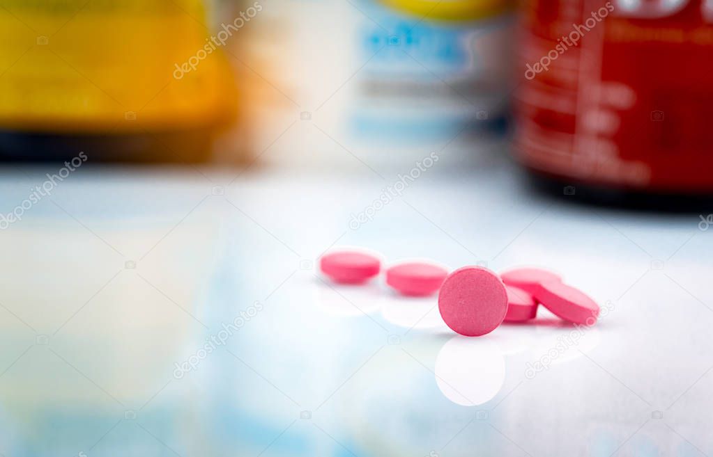Round pink tablets pill on blurred background of drug bottle. Painkiller medicine. Drug use for treatment migraine headache. Pharmacy products. Pharmaceutical industry. Drug use in daily life.
