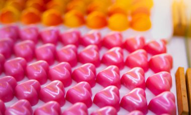 Pembe Kalp şekli çikolata. Sevgililer günü hediyesi. Beyaz plaka üzerinde Gül kokulu beyaz çikolata ganache. Çikolatalı pralin. Lüks çikolatalı şeker. Lezzetli tatlı. Aşk ve flört için gıda.