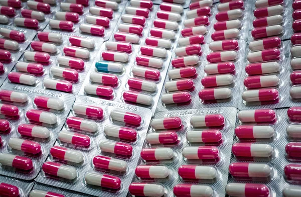 Eccezionale capsula blu-bianca in molte pillole di capsule antibiotiche rosa-bianche in blister. Resistenza agli antibiotici. Industria farmaceutica. Sanità globale. Prodotti farmaceutici . — Foto Stock