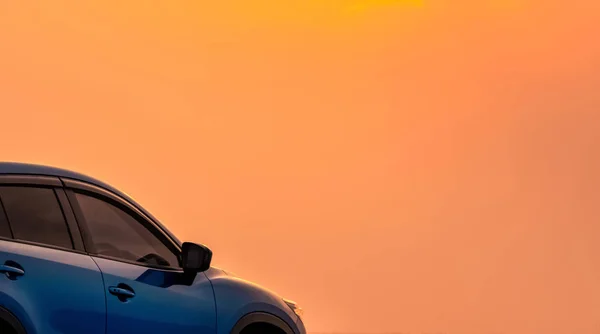 Coche SUV azul compacto con diseño deportivo y moderno estacionado junto al mar con hermoso cielo naranja al atardecer. Viaje por carretera. Tecnología y negocio de coches eléctricos. Industria automovilística y automovilística híbrida . — Foto de Stock