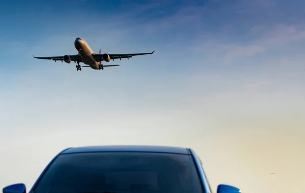 Commercial airline. Passenger plane landing approach blue SUV car at airport with blue sky and clouds at sunset. Arrival flight. Vacation time. Happy trip. Airplane flying on bright sky. Car parked.