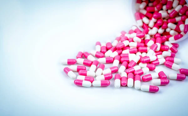 Pink and white capsules pill spilled out from white plastic bottle container. Global healthcare concept. Antibiotics drug resistance. Antimicrobial capsule pills. Pharmaceutical industry. Pharmacy.