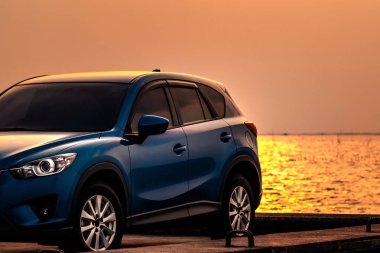 Mavi kompakt Suv araç spor ve modern tasarımı ile deniz yoluyla Beton yol üzerinde günbatımında Park. Çevre dostu teknoloji. Hibrit ve elektrikli otomobil teknolojisi. Araba park yeri. Yaz seyahat.