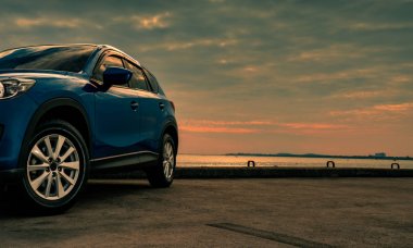Mavi kompakt Suv araç spor ve modern tasarımı ile akşam günbatımında denizin kenarında beton yolda park etmiş. Hibrit ve elektrikli otomobil teknoloji kavramı. Araba park yeri. Otomotiv Sanayi. 