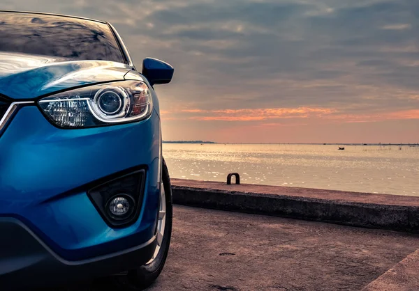 Coche SUV azul compacto con diseño deportivo y moderno estacionado en carretera de hormigón junto al mar al atardecer por la noche. Concepto de tecnología de coche híbrido y eléctrico. Plaza de aparcamiento. Industria automotriz . — Foto de Stock