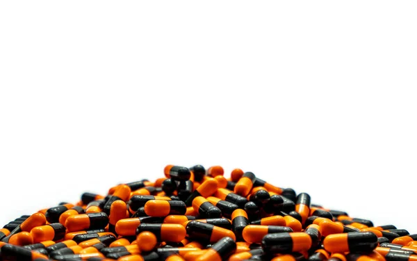 Montón de primer plano de píldoras cápsula de color naranja-negro sobre fondo blanco. Vitaminas y suplementos. Industria farmacéutica. Concepto de salud global. Producción de pastillas para cápsulas. Uso excesivo de drogas en el sistema de salud . — Foto de Stock